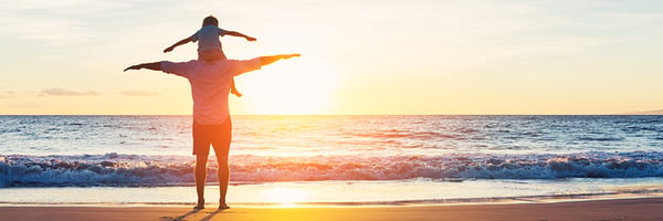 Father with son on shoulders at the beach during sunset.